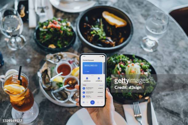close up of woman's hand managing online banking with mobile app on smartphone. tracking and planning spending. transferring money, paying bills, checking balance while dining in restaurant. technology makes life much easier - paying for dinner imagens e fotografias de stock
