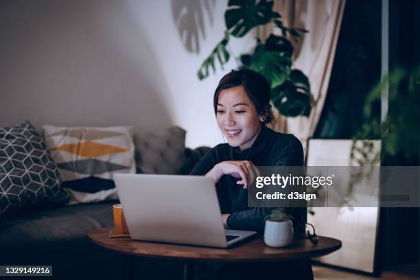 cheerful young asian woman using laptop at home till late in the evening. lifestyle and technology concept - frau am laptop stock-fotos und bilder