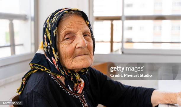 ältere frau, die allein sitzt und in die kamera schaut - arab old woman stock-fotos und bilder