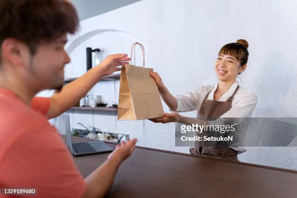 asian woman giving paper bag to customer - passing giving stock pictures, royalty-free photos & images