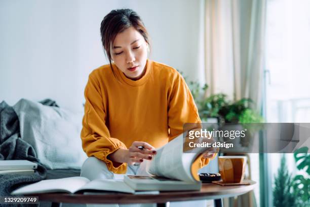 focused young asian woman reading book and making notes at home, concentrates on her studies. further education concept - lernen stock-fotos und bilder
