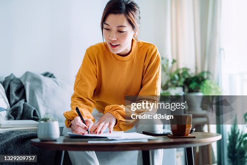 Young Asian woman holding a pen and signing paperwork in the living room at home. Deal concept Young Asian woman holding a pen and signing paperwork in the living room at home. Deal concept