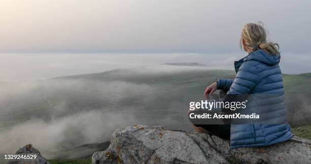 la excursionista femenina se relaja en la cresta de la montaña al amanecer - padded jacket fotografías e imágenes de stock