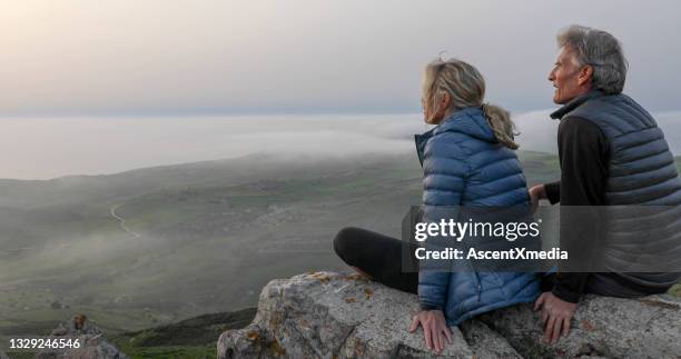mature couple relax on mountain ridge at sunrise - padded jacket 個照片及圖片檔