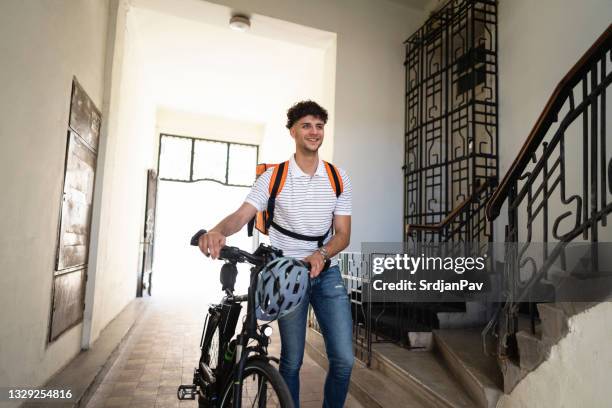 young delivery man leaving the building after delivery - apartment bike stock pictures, royalty-free photos & images
