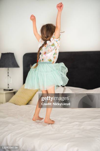 mignon petite fille sautant de haut en bas sur un lit à la maison - mini dress photos et images de collection