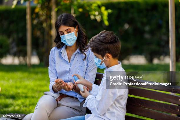 a young woman with cute son is sitting on the bench with protective masks and cleaning their hands. - antiseptic wipe stockfoto's en -beelden