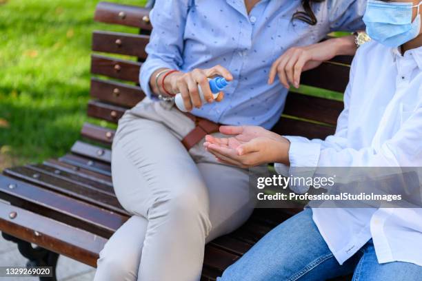 a young woman and cute son are sitting on the wooden bench with preventive measures due to coronavirus. - antiseptic wipe stockfoto's en -beelden