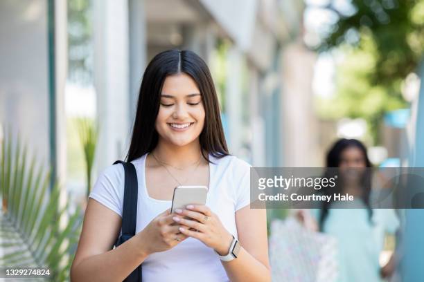 young woman uses smart phone to locate store while walking downtown - beautiful filipina stock pictures, royalty-free photos & images
