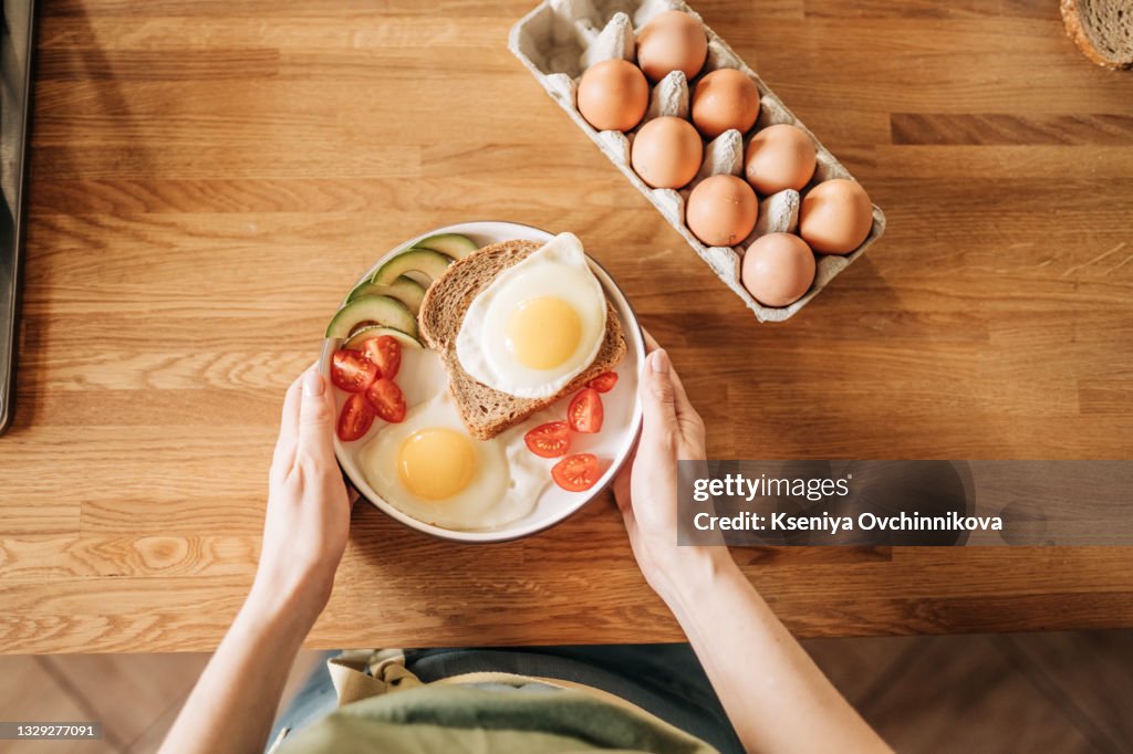 Girl hands above frying pan with three cooked eggs, herbs, cheese, tomatoes. Woman is making breakfast. top view. Copy space