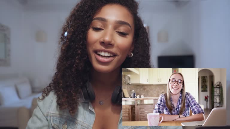 POV of beautiful young curly black Hispanic girl in with headphones on neck in video call talking and waving hand to her student friend framed low in the right. New normal distance work or lessons