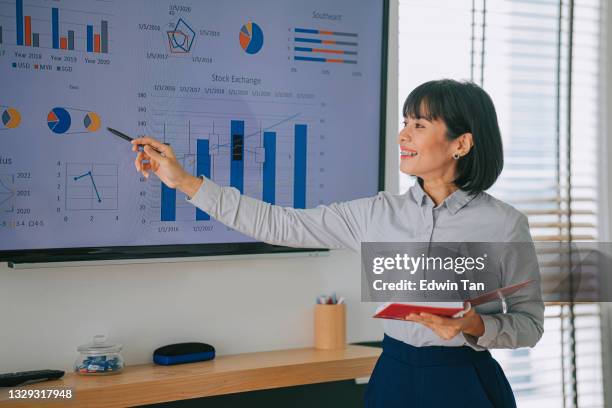 asian malay woman presenting to her colleague in conference room with television screen presentation - presenter stock pictures, royalty-free photos & images