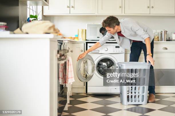 junger mann beim wäschewaschen in waschmaschine in seiner küche - wäsche stock-fotos und bilder