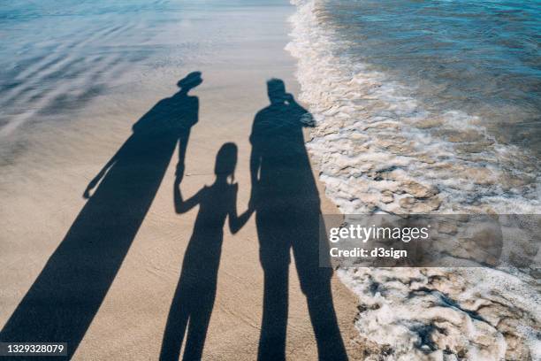 shadow on sandy beach of a loving family of three holding hands relaxing on a lovely sunny day - three girls at beach stock pictures, royalty-free photos & images