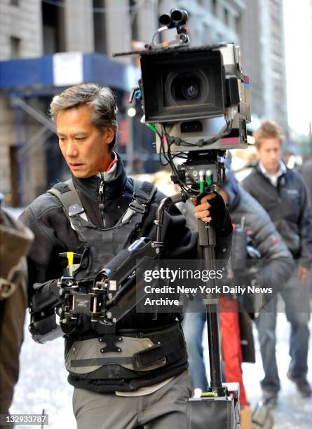 Filming of the Batman movie 'The Dark Knight Rises' at Wall Street & Williams St NYC. An Imax camera man makes his way through the organized chaos.