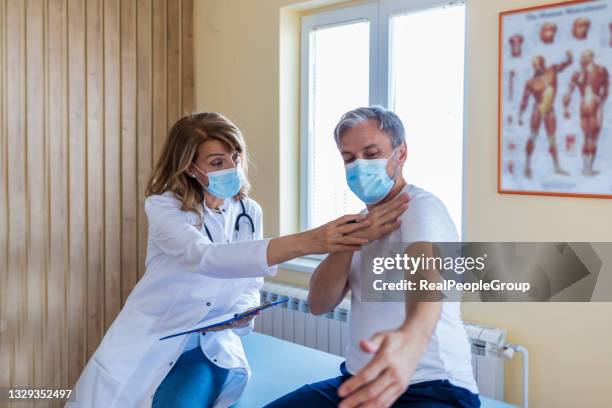 photo of a female mature  doctor with a protective face mask taking anamnesis from her mature patient - looking over his shoulder stockfoto's en -beelden