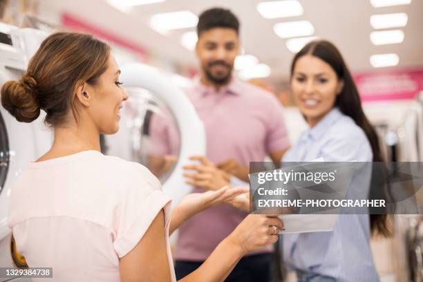 saleswoman helping young couple to choose a proper washing machine - buying washing machine stock pictures, royalty-free photos & images