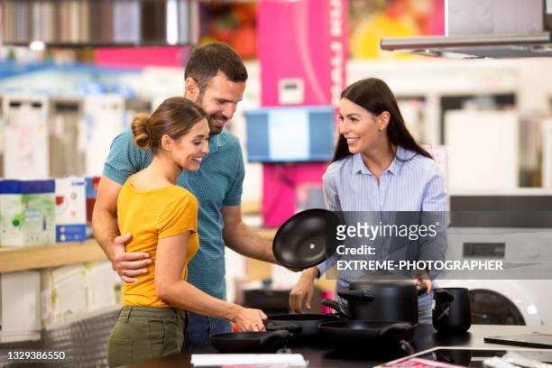 female shop assistant shows dishes to a young couple - home appliances stock pictures, royalty-free photos & images