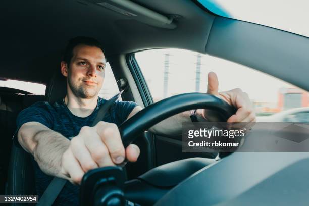 happy male driver carefree holding steering wheel of rented car with hands while driving along city street - car driver ストックフォトと画像