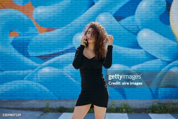 young woman talking on the phone while standing outdoors. - blue dress fotografías e imágenes de stock