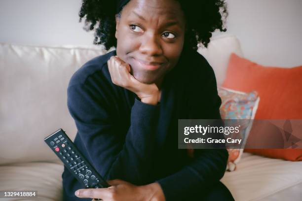 woman sits on couch watching tv - african american watching tv stock pictures, royalty-free photos & images