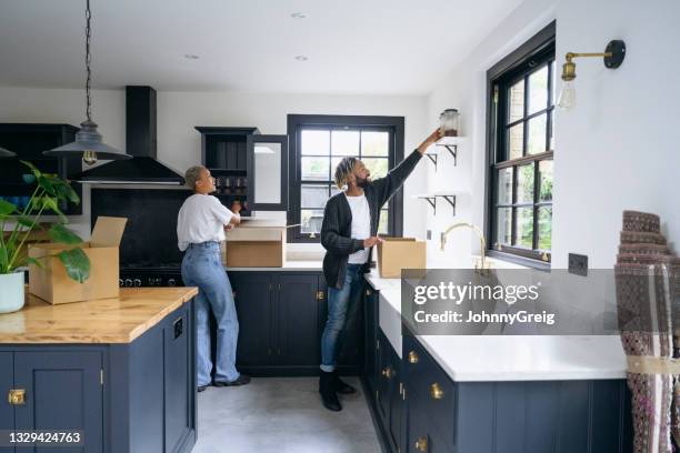 black couple unpacking boxes in shaker-style kitchen - kitchen shelves stock pictures, royalty-free photos & images