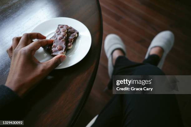 woman enjoys piece of dark chocolate with hazelnuts - barra de chocolate fotografías e imágenes de stock