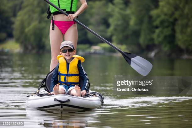 mother and son stand up paddle-boarding on quiet lake during a warm sunny summer vacation day - sup stockfoto's en -beelden
