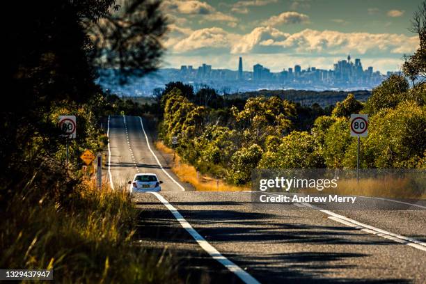 one car driving on empty road  in forest, city skyline and clouds - new south wales road stock pictures, royalty-free photos & images