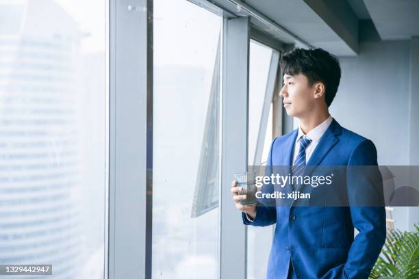 businessman holding cup water standing by office window - water cooler stockfoto's en -beelden