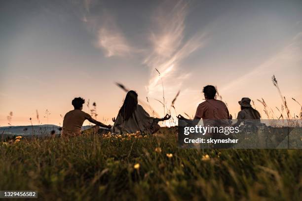 rückansicht von entspannten menschen, die bei sonnenuntergang in der natur meditieren. - meditieren stock-fotos und bilder