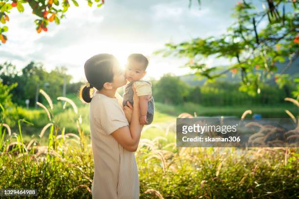 young adult asian mom embracing and carrying her daughter (2-5month ) leisure outdoor feeling joyfully - baby lachen natur stock-fotos und bilder