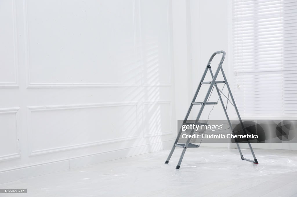 Metal stepladder on floor covered with plastic in empty room, space for text