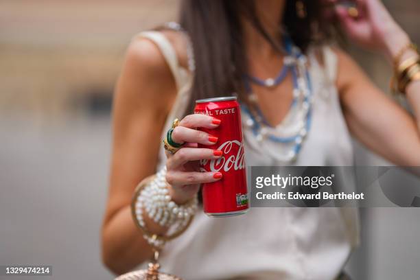 Alba Garavito Torre wears bejeweled rings and holds a Coca Colas soda drink metallic can, on July 02, 2021 in Paris, France.