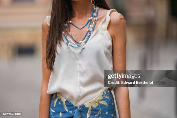 Alba Garavito Torre wears blue and silver beaded pearl necklaces, a white tank top, a pearl bracelet, a blue floral print fringed Spanish Manila...