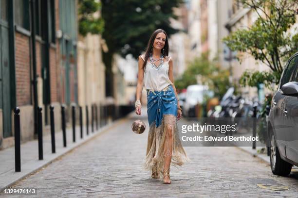 Alba Garavito Torre wears blue and silver beaded pearl necklaces, a white tank top, a pearl bracelet, a blue floral print fringed Spanish Manila...