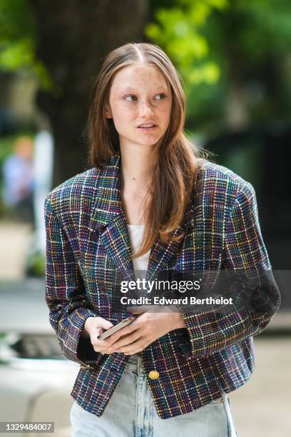 Model wears a white t-shirt, a blue / yellow / black / red checkered pattern tweed jacket, blue faded denim jeans flared pants, outside Dior, during...