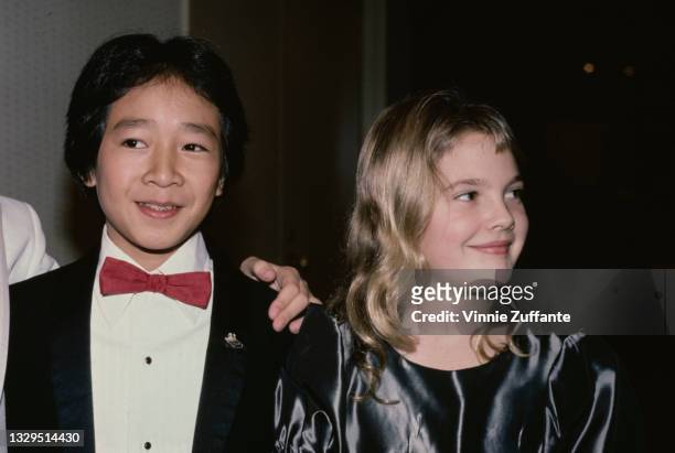 American actor Ke Huy Quan, wearing a tuxedo with a red bow tie, and American actress Drew Barrymore, wearing a grey silk outfit with a round...