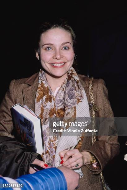 American actress Priscilla Barnes wearing a scarf and a brown jacket, a large-format book under her right arm, location unspecified, February 1982.