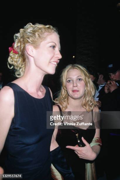 American actress Jenna Elfman, wearing a black sleeveless outfit with a red bow in her hair, and American actress Drew Barrymore, wearing a black...