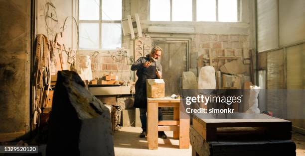 stonemason chiselling a block of stone in workshop - marble sculpture stock pictures, royalty-free photos & images