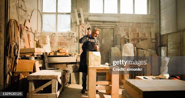 stonemason chiselling a block of stone in workshop - sculptor stock pictures, royalty-free photos & images