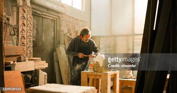 stonemason carving stone with an electric chisel in his studio - marble sculpture stock pictures, royalty-free photos & images
