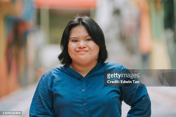 glückliche asiatisch-malaiisches Autismus-Down-Syndrom Weiblich, die in der Stadt in die Kamera schaut lächelnd in der Stadtstraße