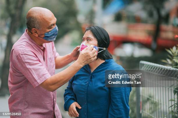 asian malay retired father helping his down syndrome daughter wearing protective face mask at city street - covid persons with disabilities stock pictures, royalty-free photos & images