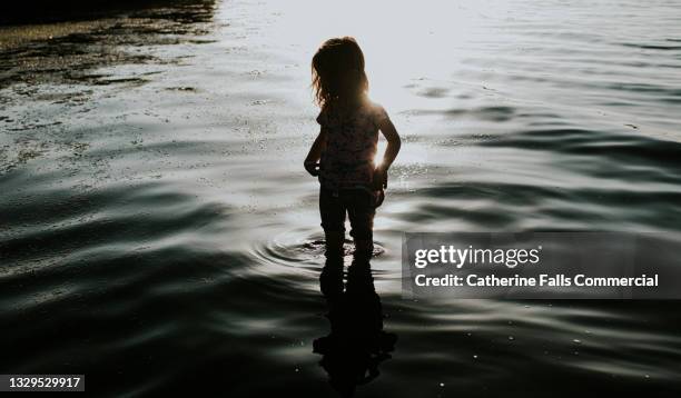 silhouette of a child in a lake, hitching up her dress - saturated color stock pictures, royalty-free photos & images