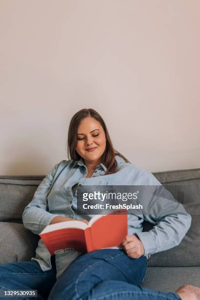 hermosa mujer de talla grande relajándose en el sofá y leyendo un libro - hourglass books fotograf�ías e imágenes de stock