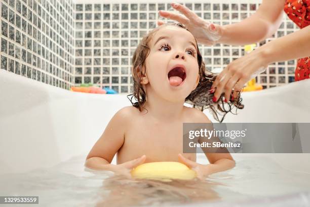 a girl is holding a sponge in the bathtub - kids taking a shower stockfoto's en -beelden