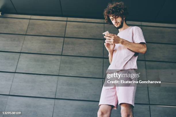 a young man with curly long hair in a pink t-shirt is typing on the phone - man side way looking stock pictures, royalty-free photos & images