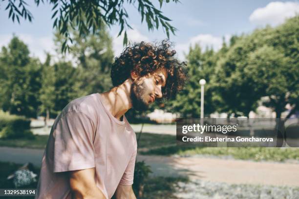 portrait of a young man 20 years old with curly hair in a pink t-shirt on a tree background - 20 years old dancing stock-fotos und bilder